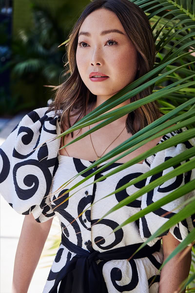 Vibrant portrait of a woman in a black and white patterned dress surrounded by lush green tropical leaves, showcasing professional fashion and portrait photography by Pamela Hanson.