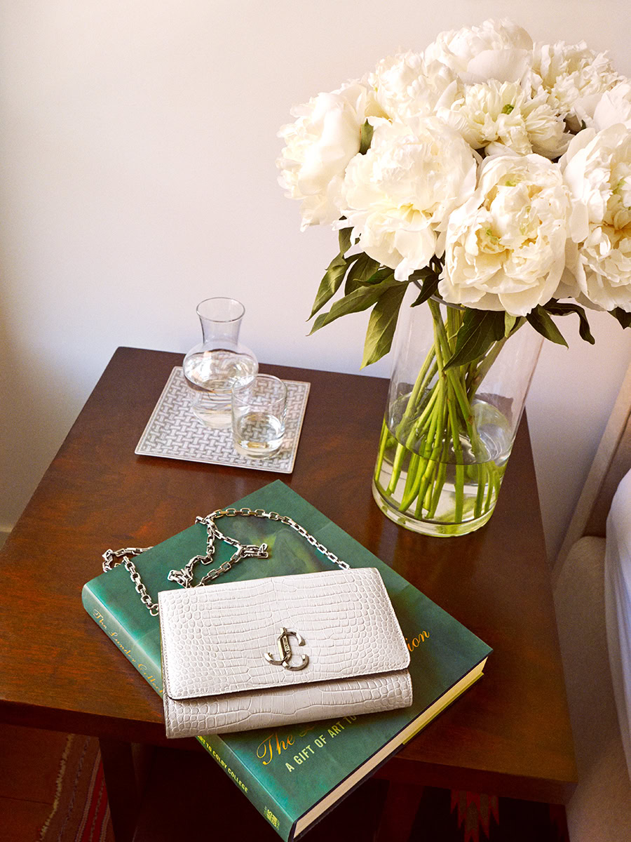 Luxury fashion accessories on wooden table with white peony bouquet in glass vase - Pamela Hanson photography.