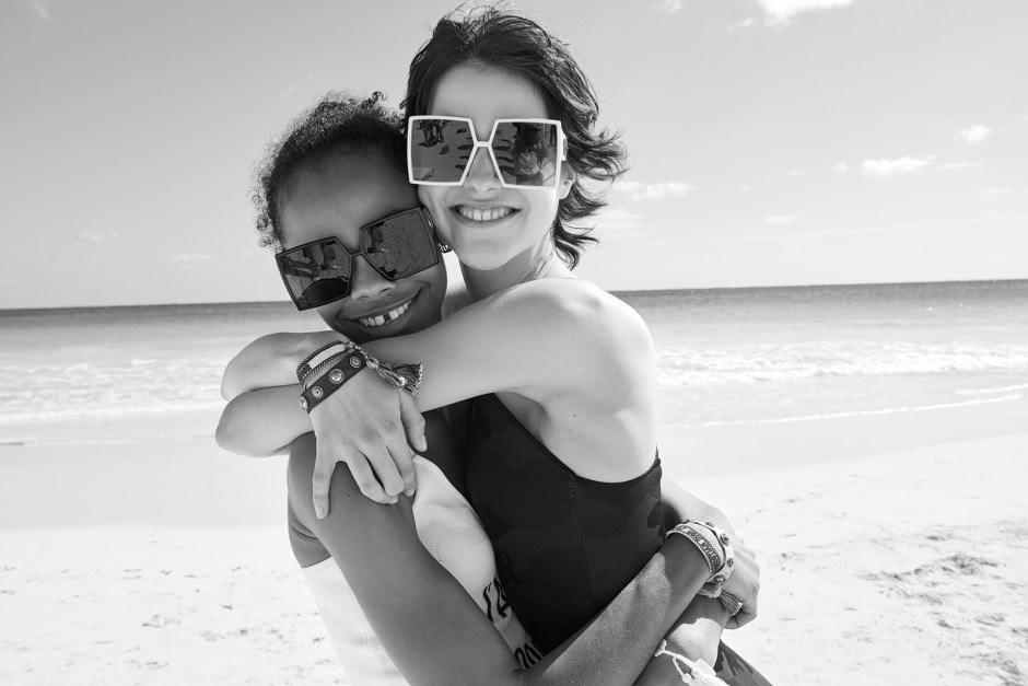 Vibrant black and white portrait of two women embracing on a sunlit beach, showcasing modern fashion, joyful friendship, and scenic seaside background in professional photography by Pamela Hanson.