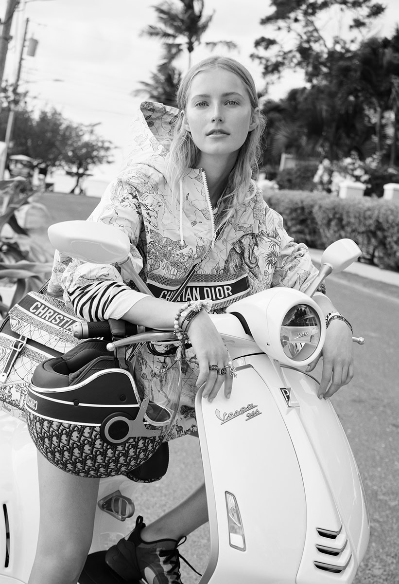 Elegant woman posing on a Vespa scooter with stylish accessories, outdoors in a tropical setting, showcasing fashionable urban lifestyle photography.
