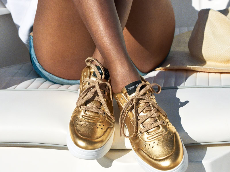 Golden metallic sneakers paired with denim shorts, captured in a vibrant outdoor setting, showcasing luxurious fashion and style photography.