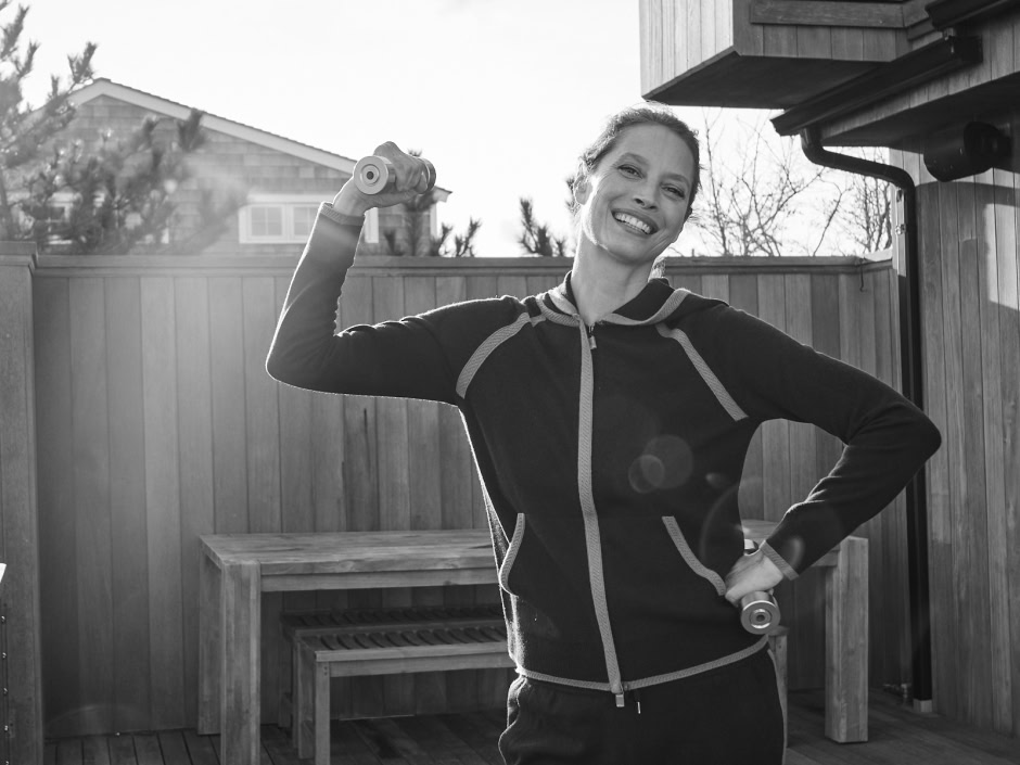 Fit woman exercising with dumbbells outdoors, smiling happily, in a backyard setting, black and white photo capturing health and wellness lifestyle.