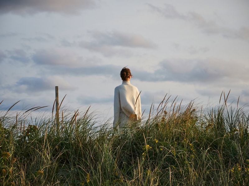 Serene woman standing in tall grass during sunset, capturing tranquil outdoor photography by Pamela Hanson.