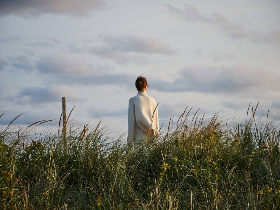 Serene woman standing in tall grass during sunset, capturing tranquil outdoor photography by Pamela Hanson.