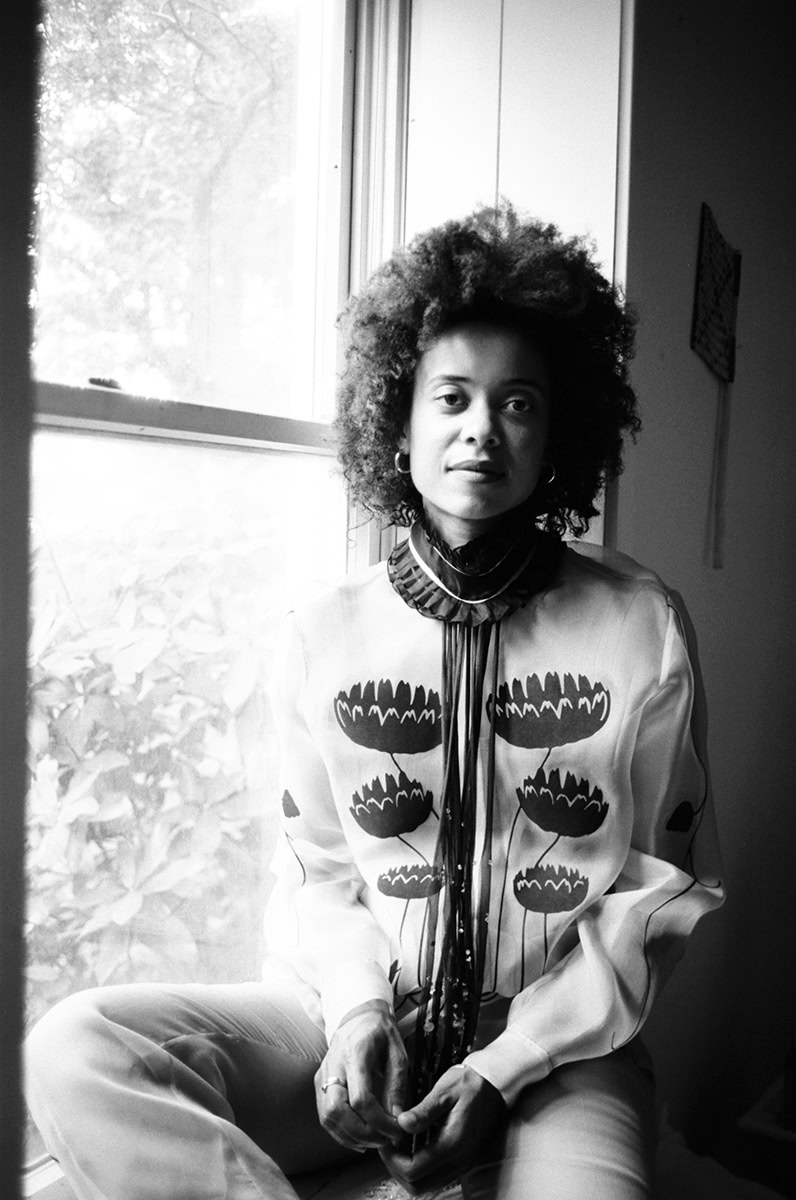 Portrait of a woman with natural curly hair in black and white, sitting near window, photography by Pamela Hanson, artistic black and white portrait, fine art photography, elegant and expressive lady, modern portraiture.