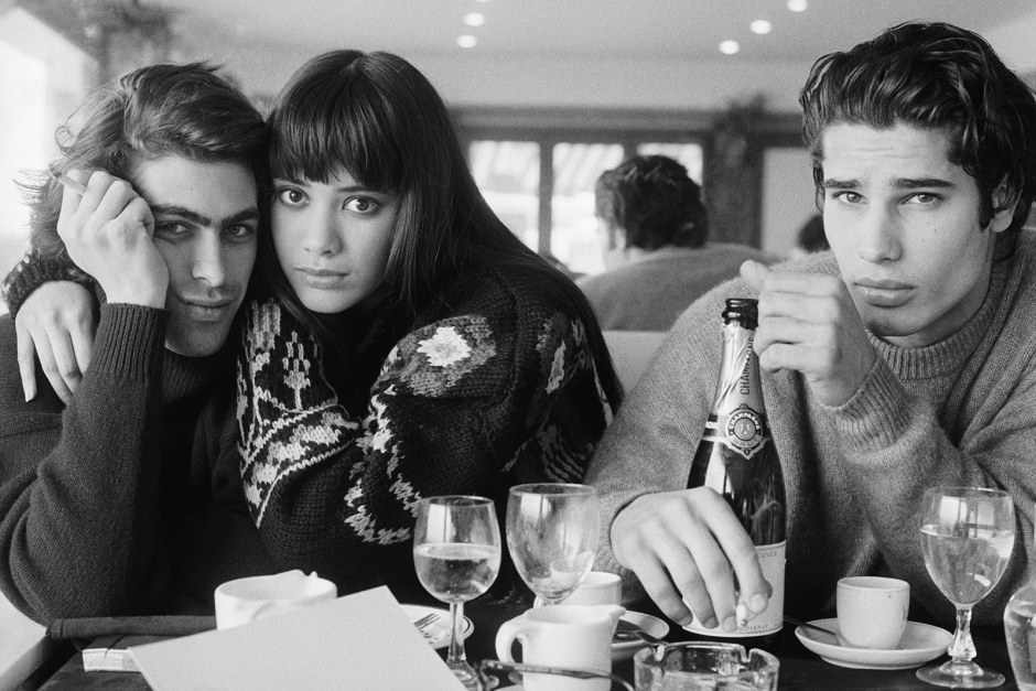 Elegant black and white portrait of three young adults sitting at a dining table, featuring intense expressions, stylish clothing, and classic tableware, showcasing fine art portrait photography by Pamela Hanson.