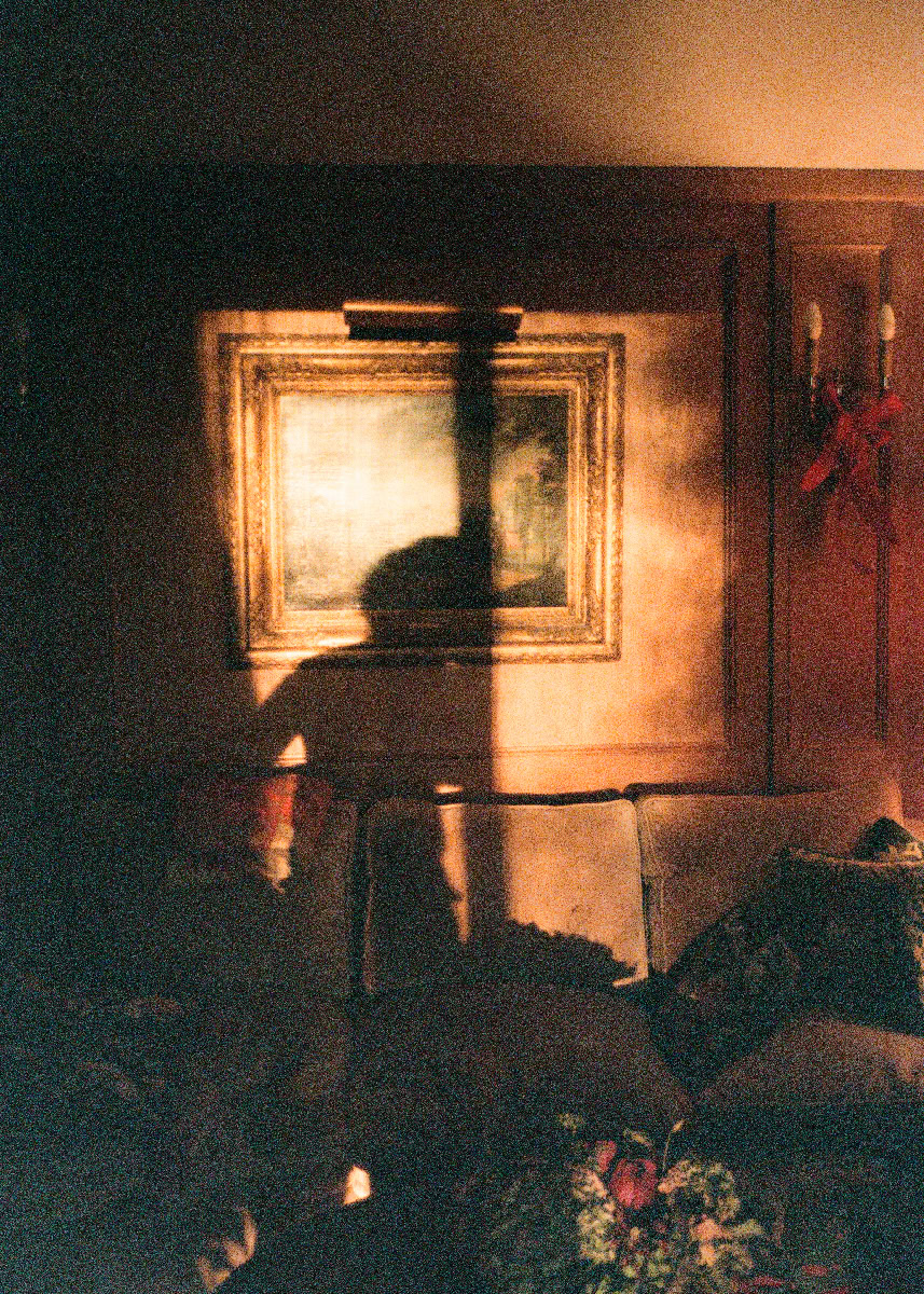 Silhouette of a woman with a raised arm in warm, ambient indoor lighting, framed by classic wall art and cozy furnishings, capturing artistic and intimate moments in photography.
