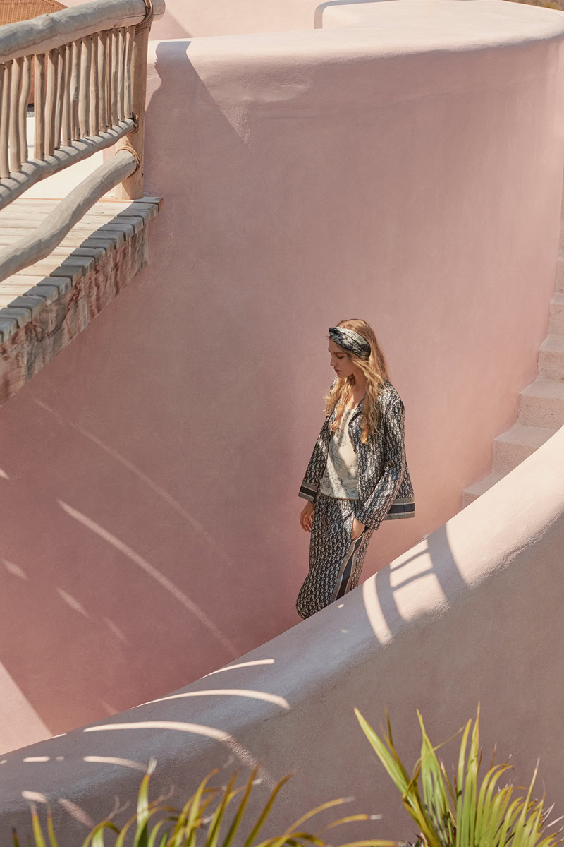 Elegant woman in patterned clothing walking down pink stucco stairs at Pamela Hanson Photography shoot, showcasing fashion and lifestyle photography with artistic urban backgrounds.