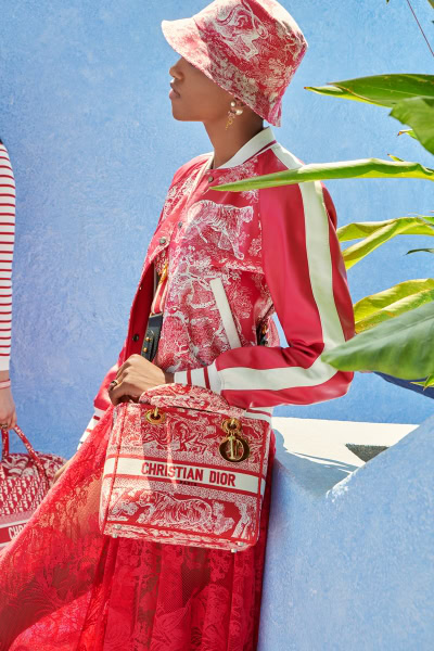Elegant fashion portrait of a woman in a vibrant Christian Dior outfit with a matching bag, set against a bright blue Mediterranean-style background, showcasing high-end luxury fashion photography.