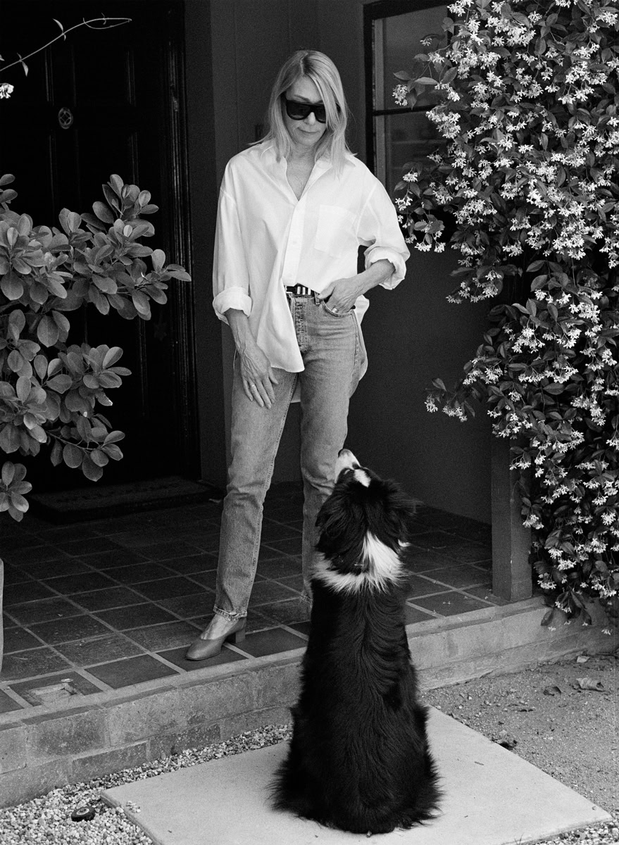 Elegant woman in casual outfit with dog at doorway, black and white portrait, modern lifestyle photography, outdoors.