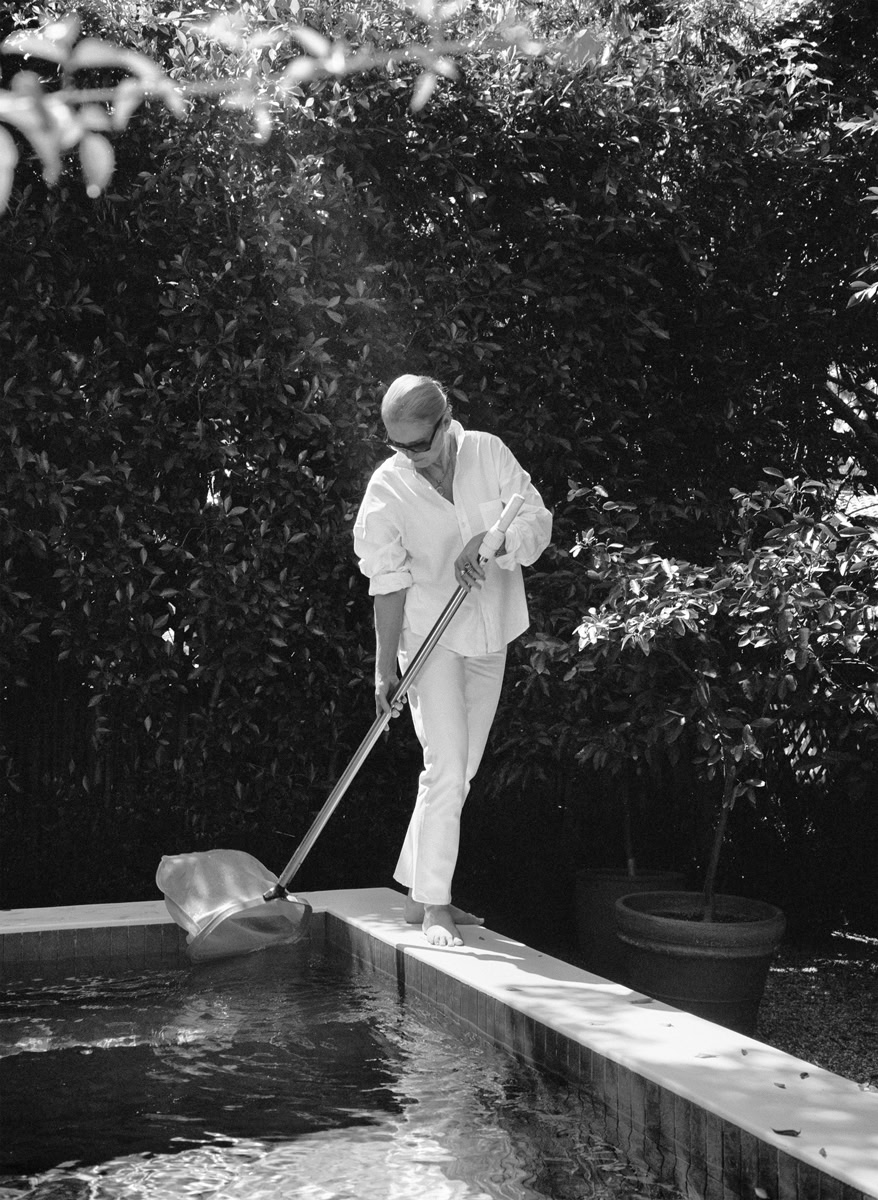 Swan woman in white dress cleaning reflecting in a pool, black and white artistic photography, elegant water scene, outdoor poolside portrait, sophisticated lifestyle photography.