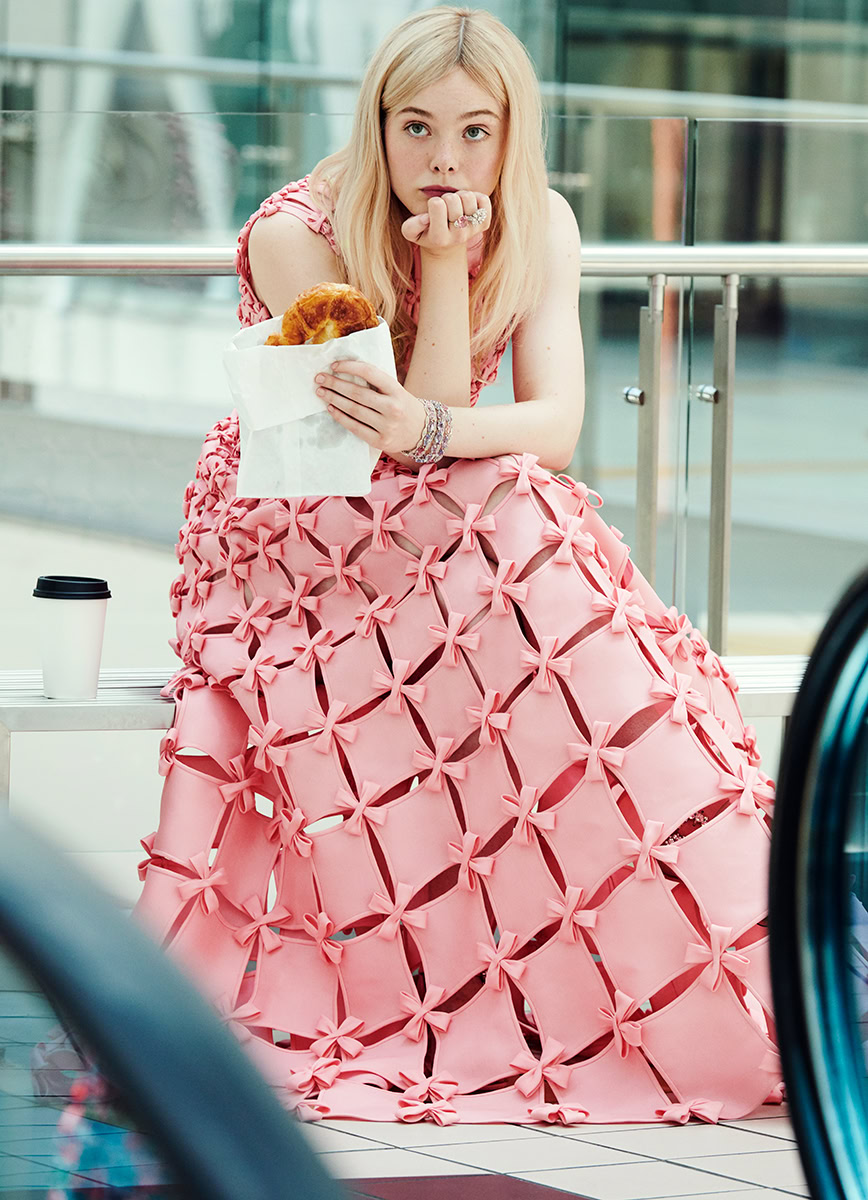 Pink fashion photography of a young woman in a pink dress with a bow design, sitting in an airport with food and coffee, captured by Pamela Hanson Photography.
