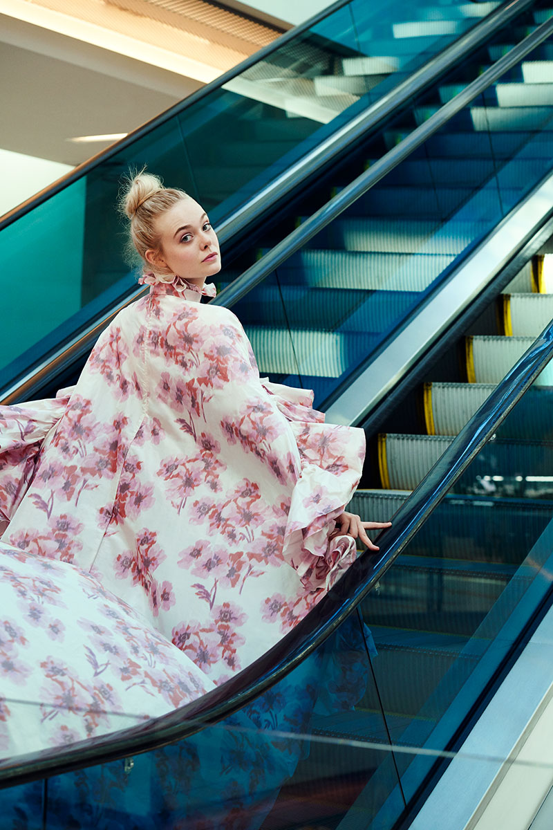Elegant woman on escalator wearing floral dress in modern shopping mall, fashion photography, contemporary style.
