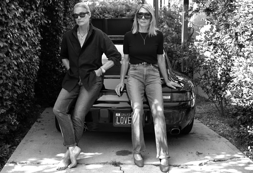 Elegant women in casual denim outfits posing outdoors near a sports car, black and white photography emphasizing timeless fashion and photography art.