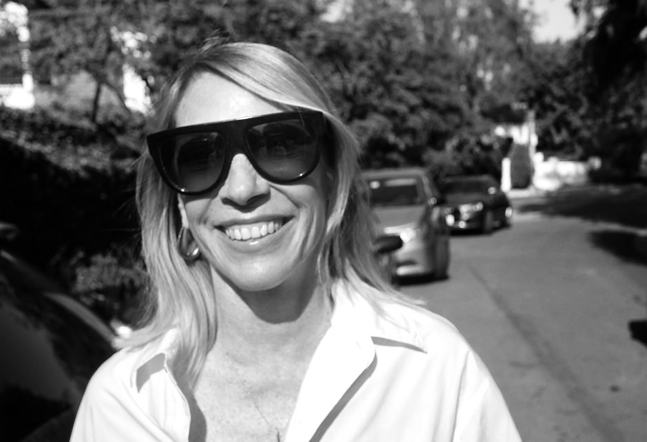 A woman smiling outdoors wearing large sunglasses, captured in black and white by Pamela Hanson Photography.