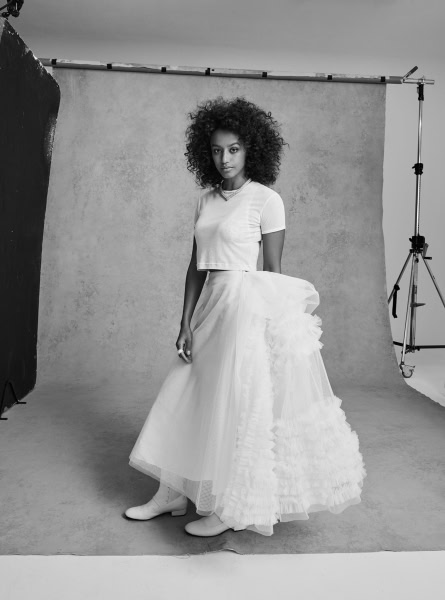 Black and white portrait of a young woman with curly hair in a professional photography studio, wearing a casual crop top and a voluminous layered skirt, capturing fashion and beauty photography concepts, Pamela Hanson Photography.