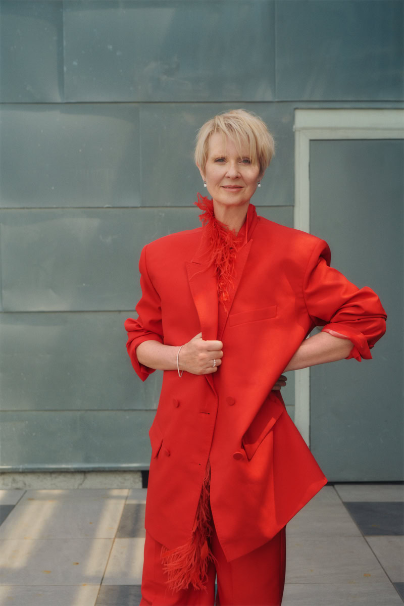 Elegant woman in vibrant red suit with feather details, outdoor portrait, professional fashion photography, modern background, stylish and confident look.
