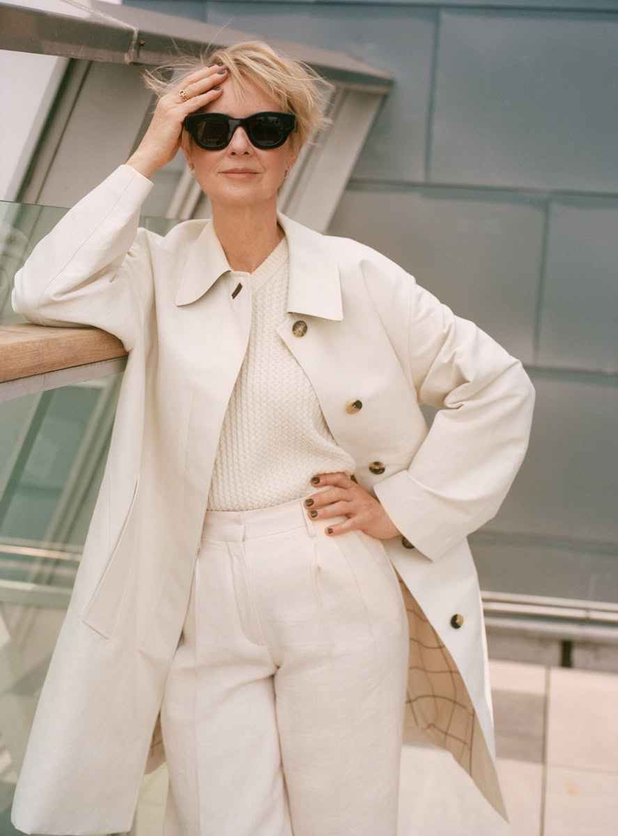 Elegant mature woman in white trench coat and sunglasses, fashion portrait, modern urban setting, stylish and confident, Pamela Hanson Photography.