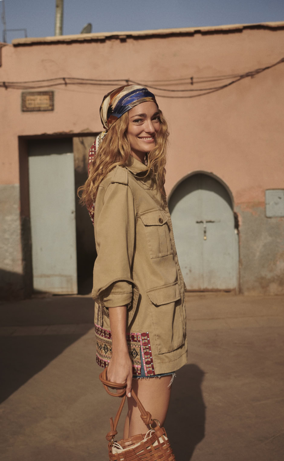Colorful headscarf and casual beige jacket in warm sunlight, urban street scene with pastel building background, fashion photography by Pamela Hanson.