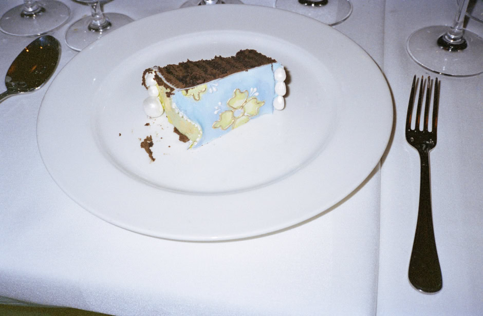 Miniature decorative cake with blue floral icing on a white plate at an elegant dining table.
