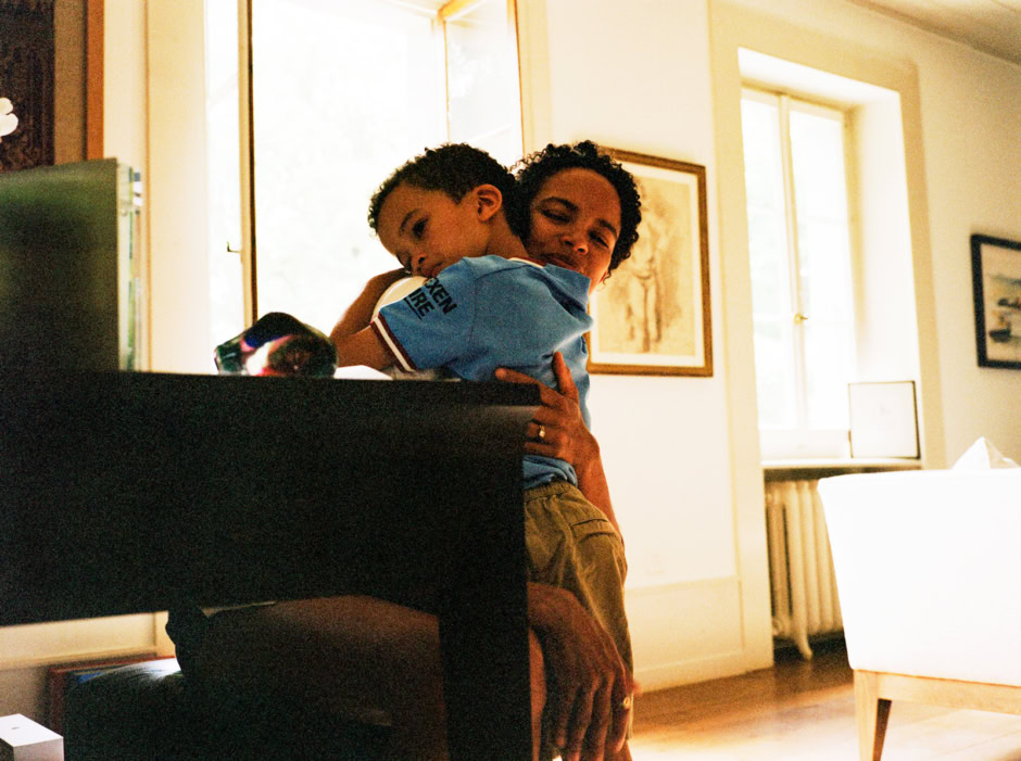 A woman holding a young boy in a cozy indoor setting, capturing a candid and intimate moment with natural light from large windows, showcasing emotional connection and warmth.
