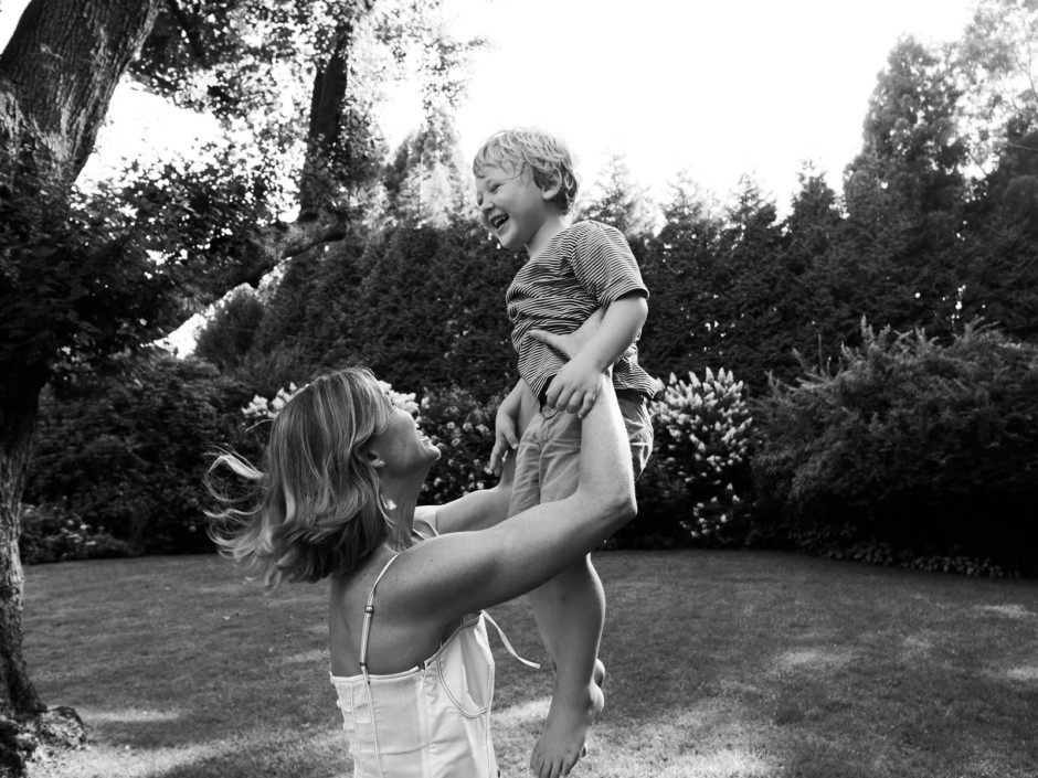 Joyful mother lifting her son outdoors in a sunlit garden, capturing candid moments of happiness and connection in a natural setting.