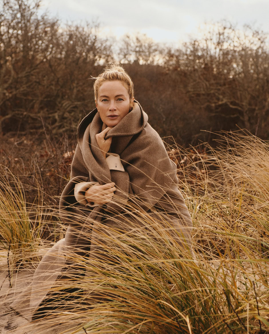 Elegant woman in a cozy coat amidst tall grasses outdoors during autumn in a professional fashion photography shoot.
