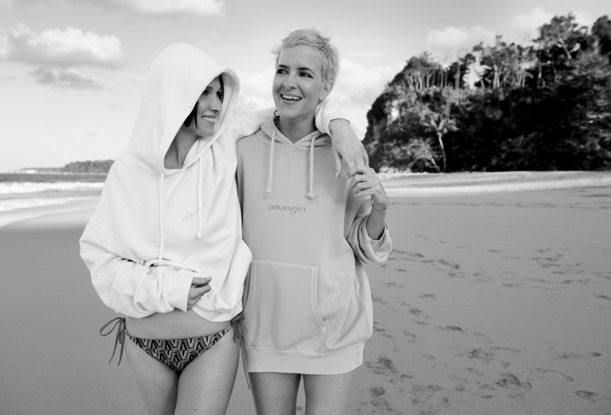Amusing black and white photo of two women enjoying a moment together on the beach in casual hoodies, showcasing Pamela Hanson Photography's focus on lifestyle, fashion, and portrait photography.