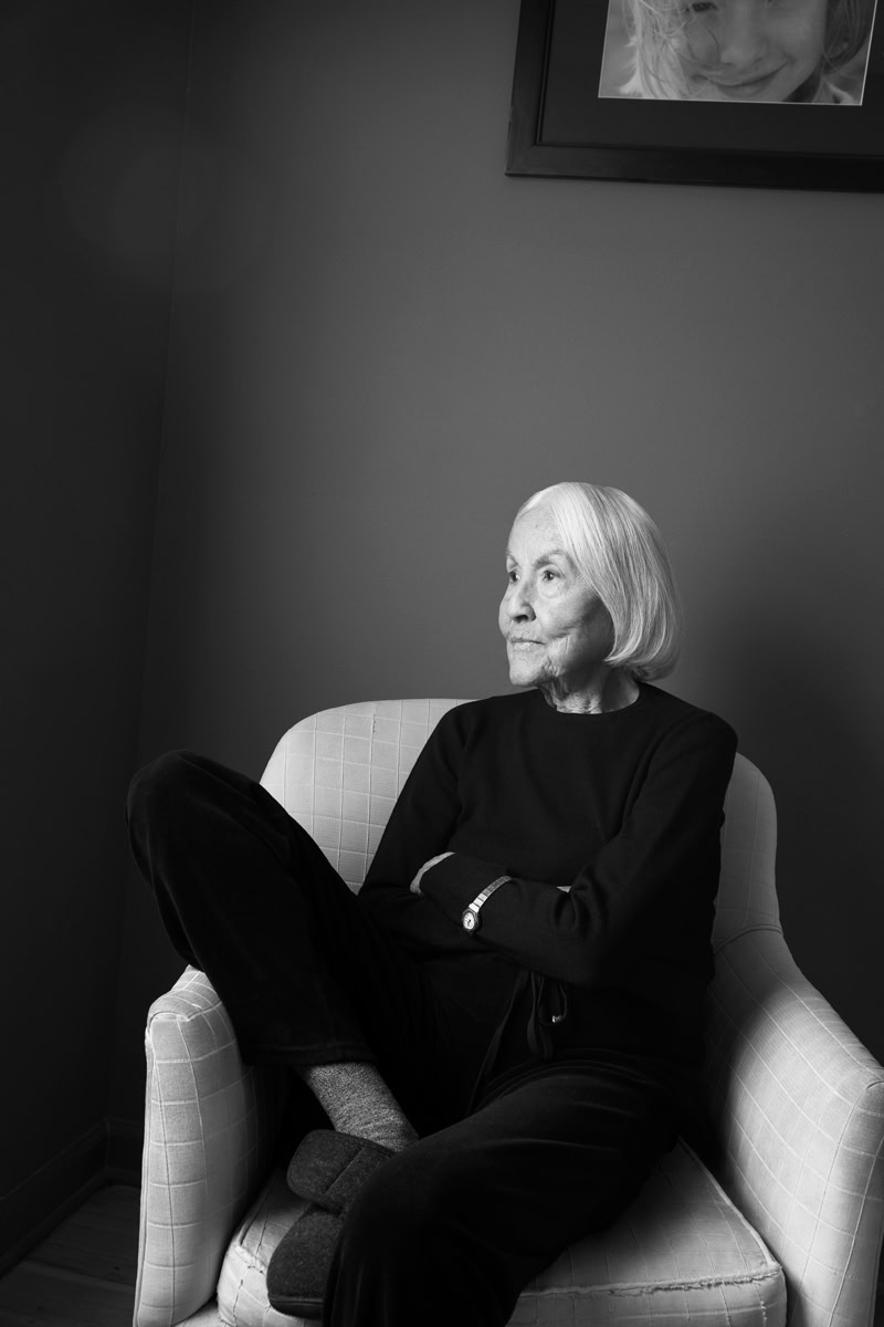 Serene elderly woman sitting in a cozy armchair, black and white portrait capturing elegance and timeless beauty.
