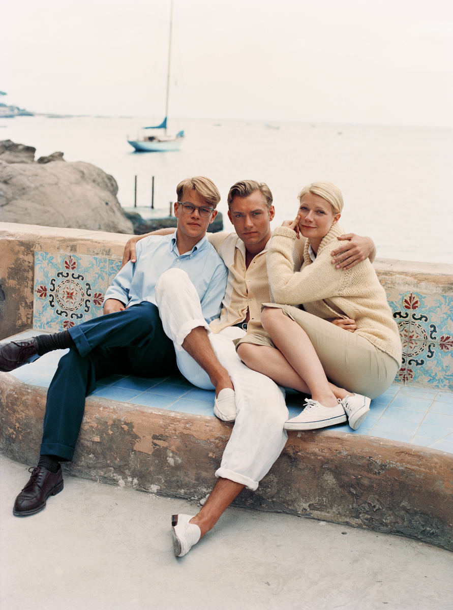 Relaxed seaside portrait of three young friends sitting together on a rustic bench near the ocean, captured by Pamela Hanson Photography, showcasing casual fashion and candid moments at a coastal location.