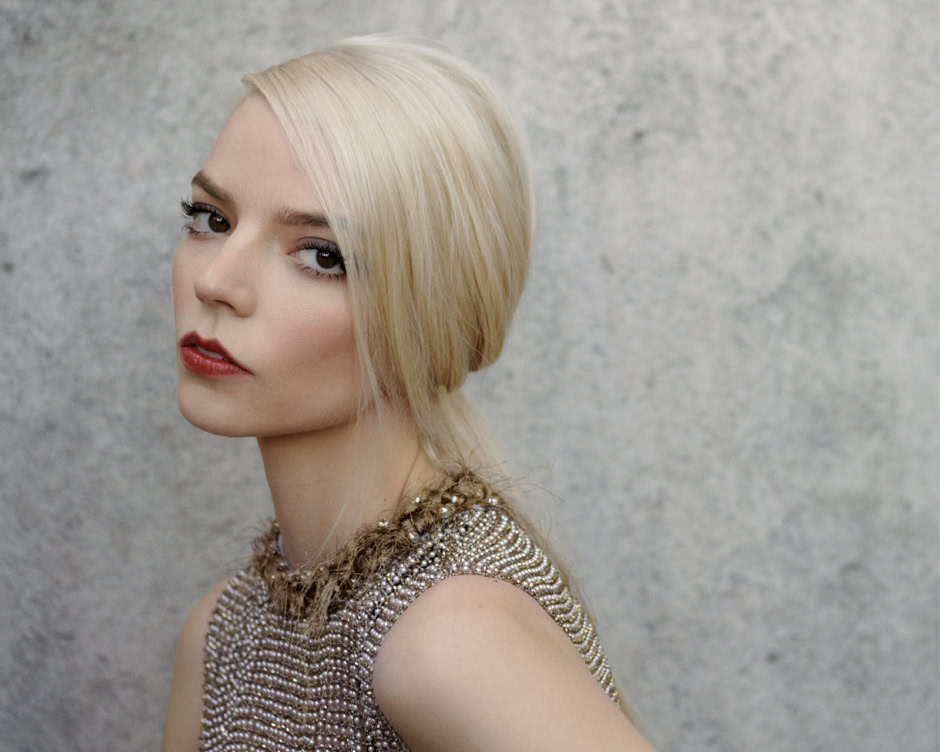 Luxury fashion portrait of a blonde woman with sleek bob hairstyle wearing a pearl beaded top against a concrete wall background.