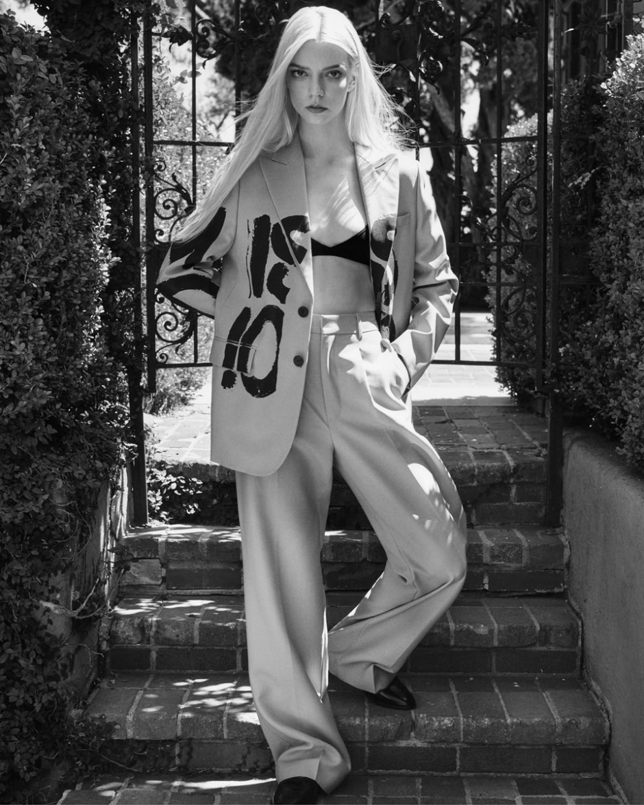 Blonde model in stylish patterned blazer and wide-leg trousers standing on brick steps outside black and white photography portrait of fashion model outdoors at garden gate.