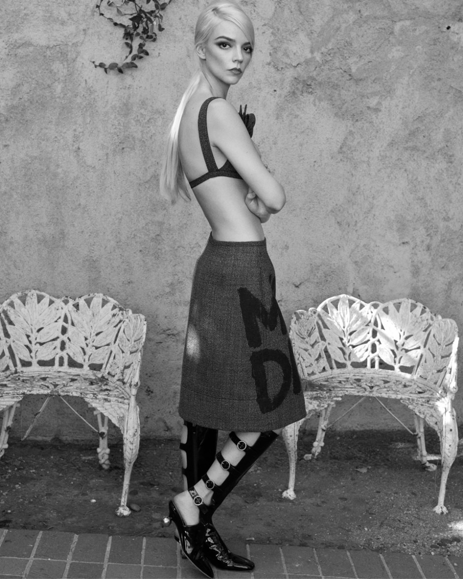 Elegant black and white fashion photography featuring a model in avant-garde attire with high heel shoes, artistic pose, and textured background, showcasing contemporary portrait styling.