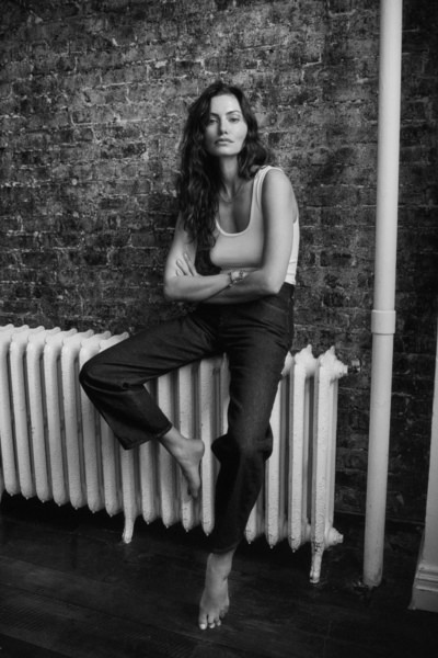 Elegant black and white portrait of a woman with wavy hair standing barefoot by a vintage radiator against an exposed brick wall, showcasing Pamela Hanson's artistic摄影works.