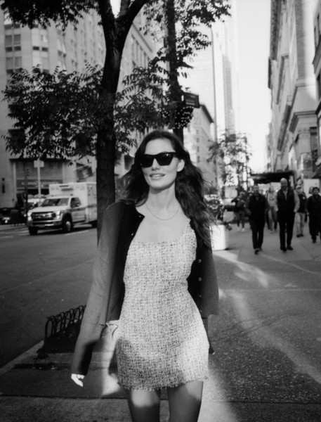 Woman walking on city street in black sunglasses and stylish dress in black and white photo.