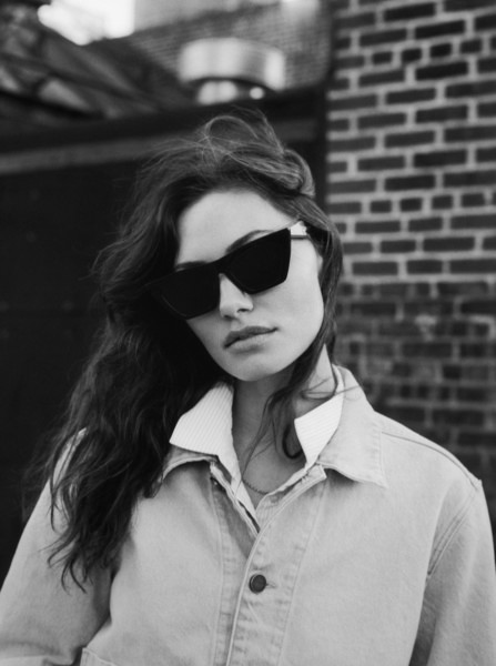 Elegant black and white portrait of a woman wearing oversized sunglasses and a classic denim jacket. Captured by Pamela Hanson Photography, emphasizing fashion, portrait, and street style photography in an urban setting.