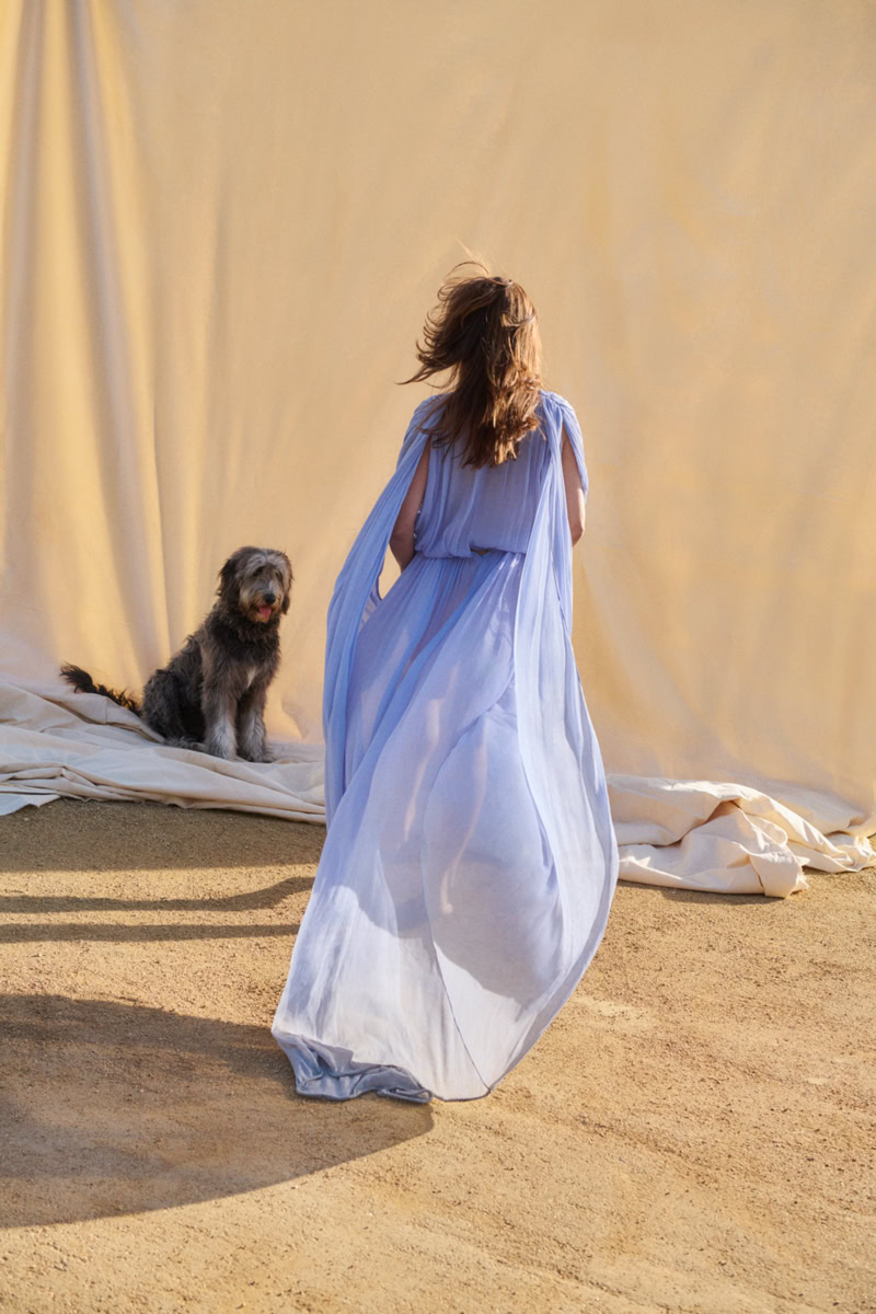 Elegant woman in flowing light blue dress with dog in a professional fashion photography setting.