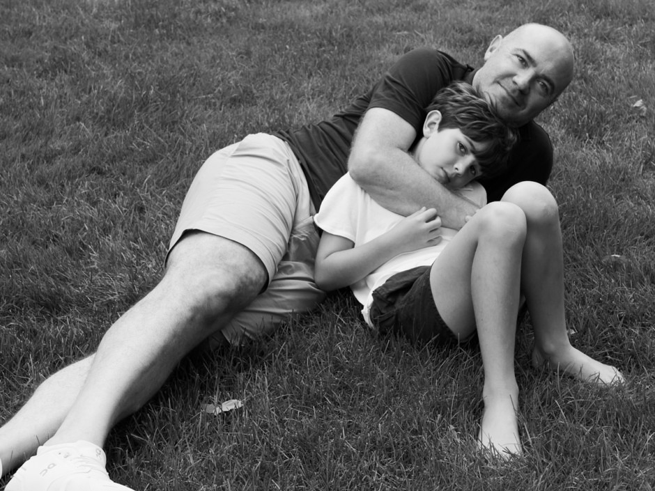 A black and white portrait of a father and daughter lying on the grass, capturing a tender moment of family connection and emotional expression in outdoor photography.
