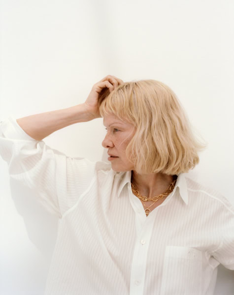 Elegant woman with blonde hair in a white shirt, minimalist portrait for fashion and beauty photography by Pamela Hanson, showcasing natural look and sophisticated style.