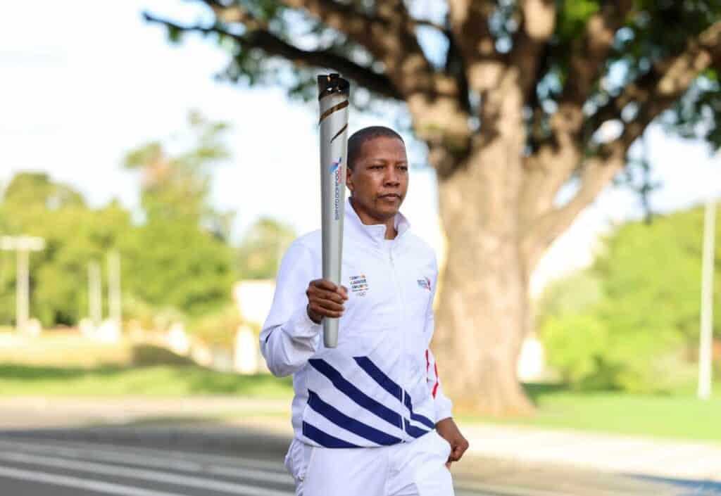 Atleta sosteniendo la antorcha de Santo Domingo 2026 en un parque al aire libre.