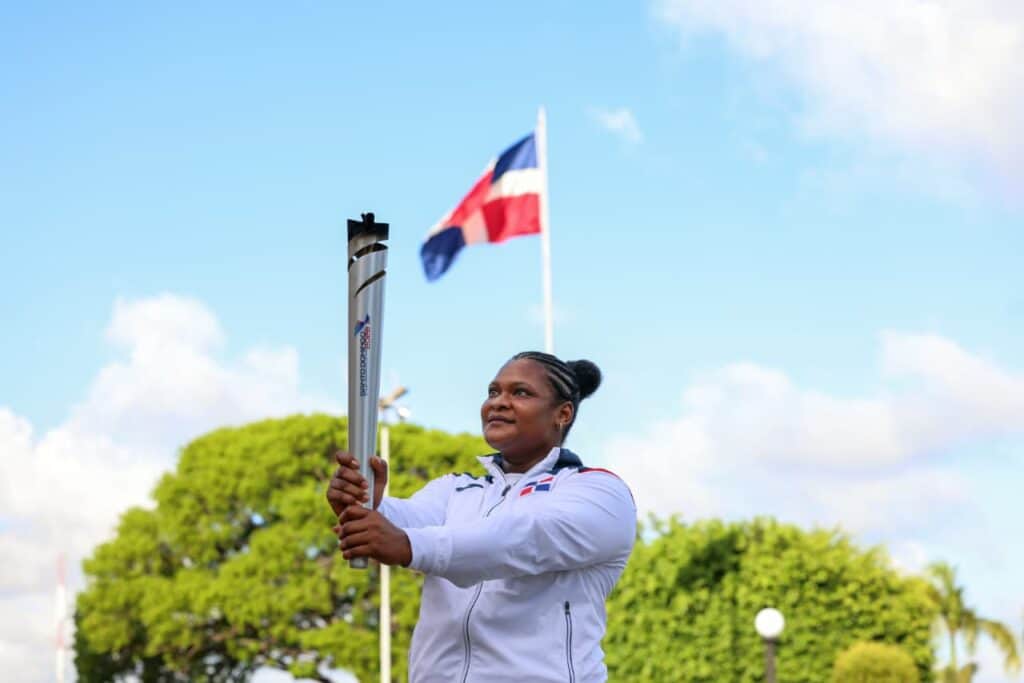 Bandera dominicana ondeando en un parque con una mujer sosteniendo un mástil, símbolo de orgullo y p.