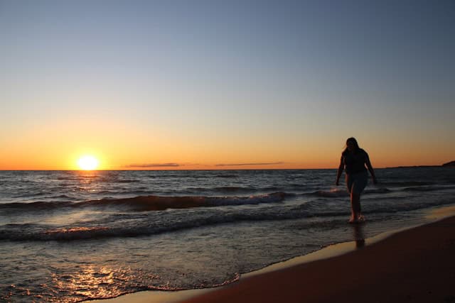 Beach in Ludington mi at sunset with woman walking by water
