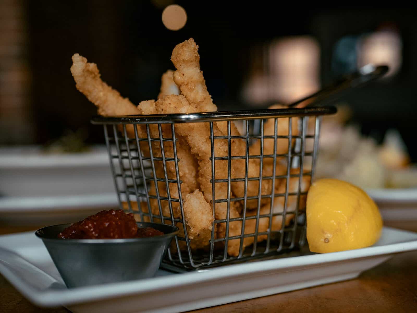 A basket of fried food on s plate with a cup ketchup and half a lemon