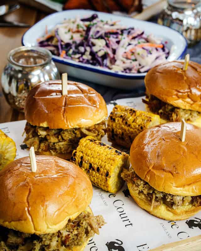 A picture of a few pork sandwiches, corn on the cob and Cole slaw