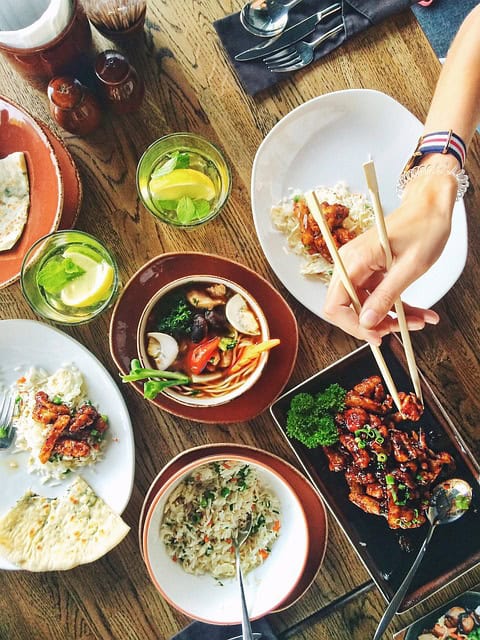 A table full of food with a hand grabbing food with chopsticks