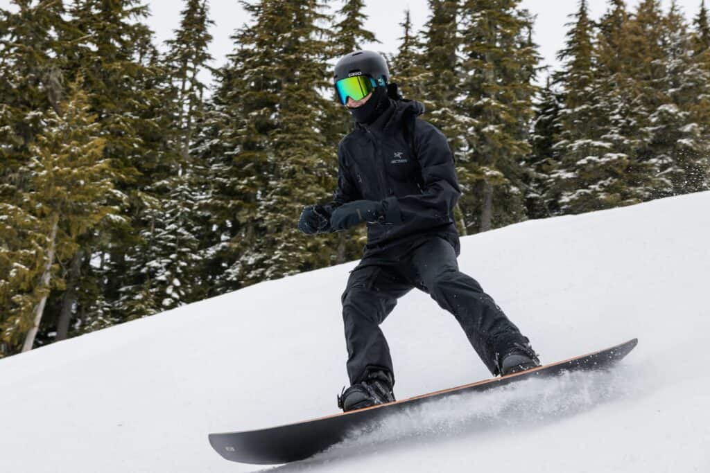 person snowboarding on snowy slope with pine trees behind them