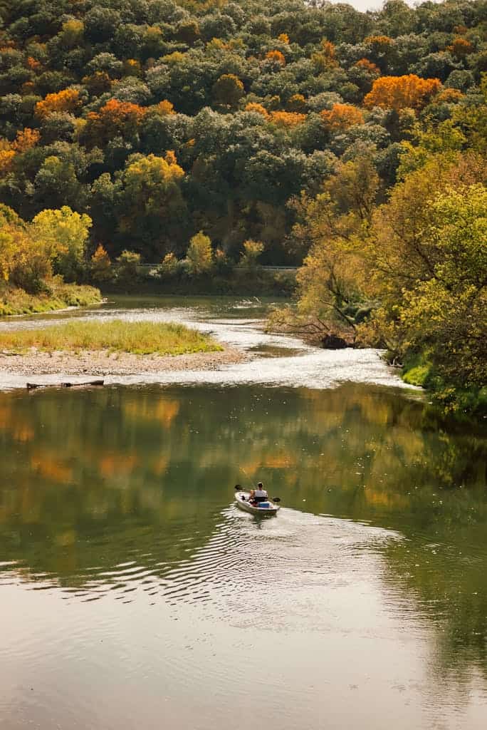 A kayaker enjoys a peaceful paddle on a scenic river surrounded by vibrant fall foliage.