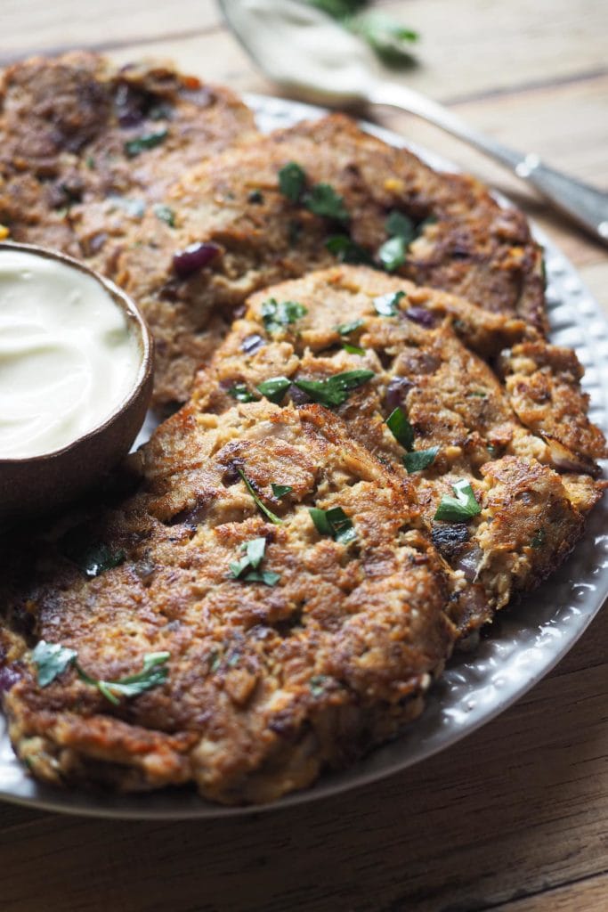 Esta receta de Hamburguesas de Atún es deliciosa, sabrosa y te salva las cenas de entre semana. Están hechas con ingredientes que siempre solemos tener en casa y también son perfectas para preparar comida con antelación! Además, es una receta sin gluten. Foto en unos 45º del plato con hamburguesas de atún y el bol de mayonesa. Al fondo se ve una cucharita con mayonesa.