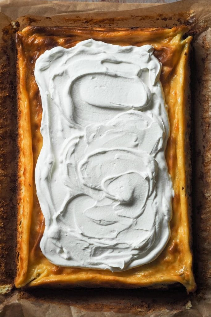 Brownie Cheesecake con Nata y Fresas. Abajo, un brownie denso y jugoso. Luego, una capa de cheesecake de vainilla y para terminar, nata montada y fresas. Y encima es fácil de hacer y (casi) imposible de liarla, te lo prometo! En la foo se ve el brownie cheesecake desde arriba con el topping de nata montada esparcido por encima de todo el cheesecake dejando los bordes sin cubrir.