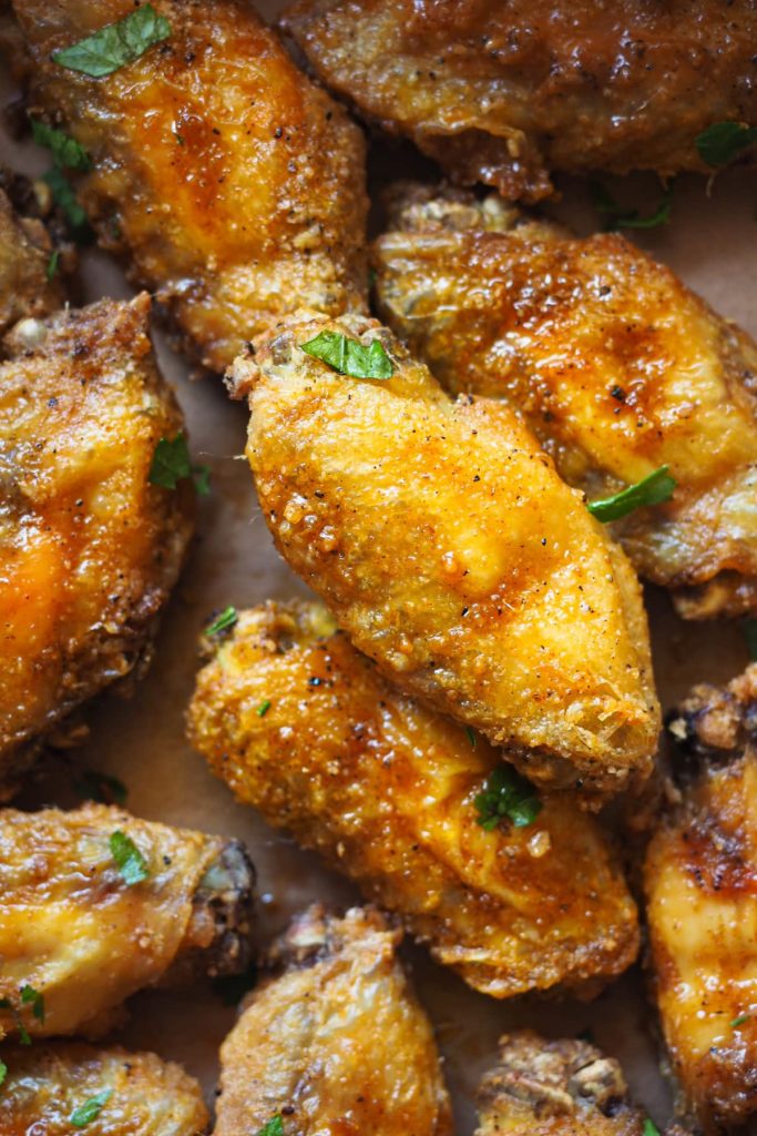 Alitas de pollo crujientes al horno adictivas. Llevan un aliño de ajo y pimentón que es, literal, para chuparse los dedos y van acompañadas de un dip de yogur y limón que balancea todos los sabores. Aquí se ven las alitas de cerca con perejil picado espolvoreado por encima.